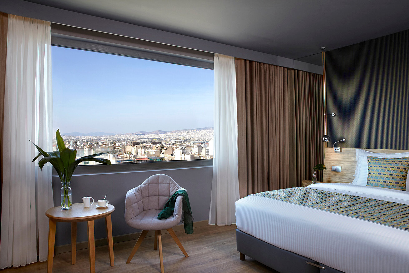 Komfortables Standardzimmer mit Schreibtisch und Blick ins Atrium des Wyndham Grand Athen