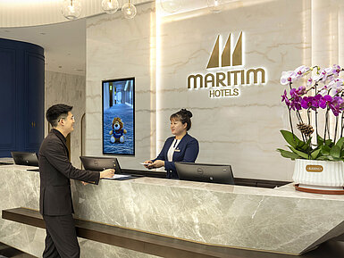 Gast im Gespräch mit Mitarbeiterin an der modernen Rezeption des Maritim Hotels