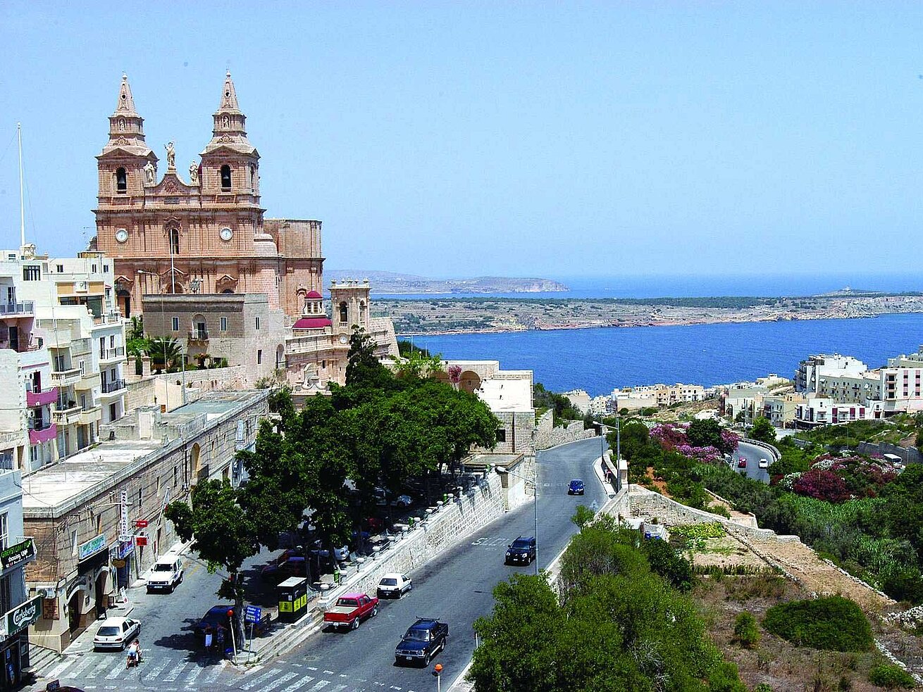 Küstenstadt mit historischer Kirche, Straße und Blick auf das blaue Meer unter klarem Himmel
